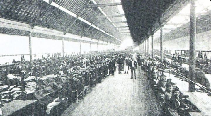 Historic photo of the long workroom floor of the Limerick Clothing Factory, rows of workers at tables under a sawtooth glass roof